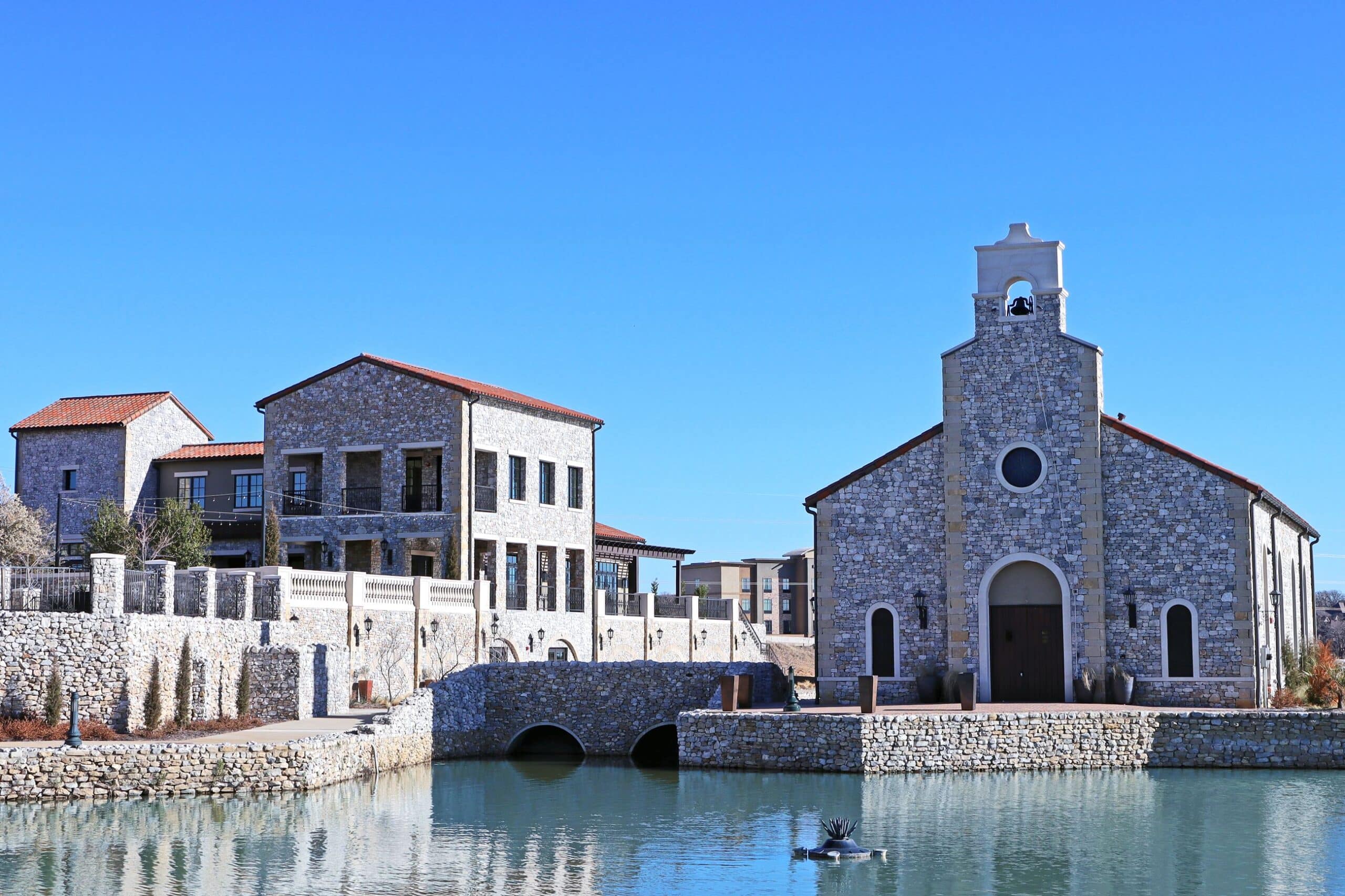 Scenic view of stone buildings and a pond in Westlake, TX, surrounded by professionally maintained landscaping, showcasing expert landscape installation by a Westlake landscape company