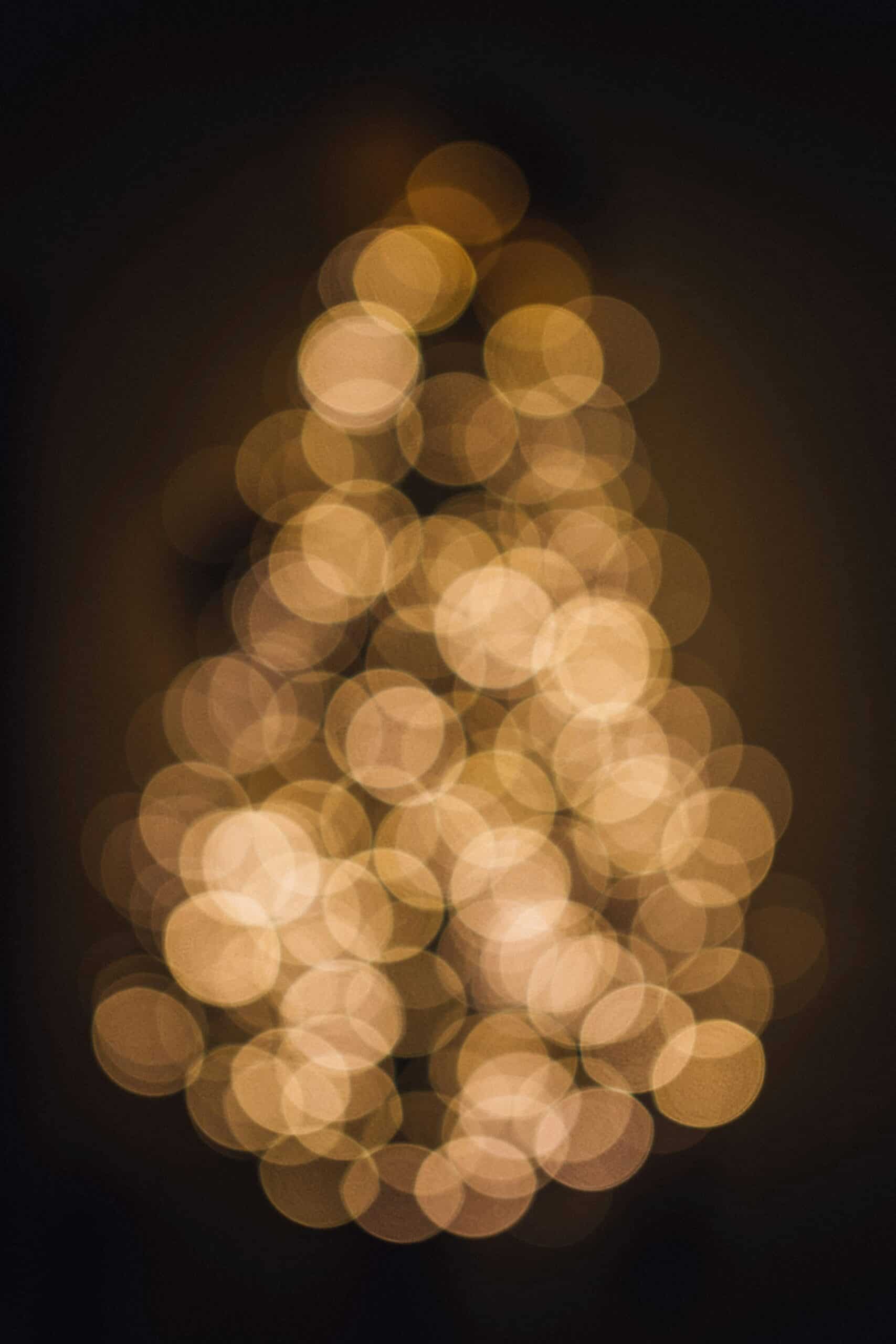 A cluster of warm, golden circular bokeh lights forms a vague, triangular shape against a dark background, resembling a blurred, glowing Christmas tree—reminiscent of Westlake Christmas lights.